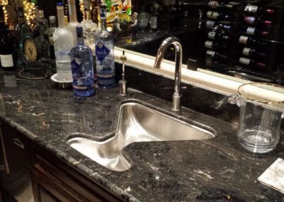 A bar counter with a sink and a bottle of wine.